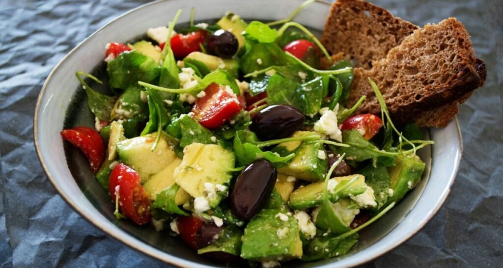 Fresh salad featuring avocado, cherry tomatoes, olives, feta cheese, and leafy greens, served with whole grain bread, highlighting a nutritious and balanced meal for weight loss.