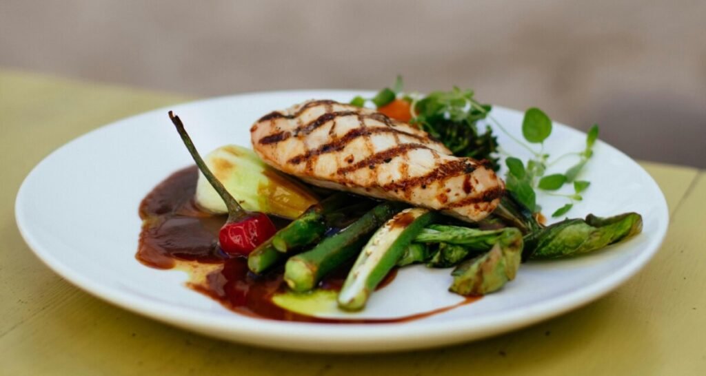 Grilled chicken served with a variety of vegetables, including asparagus and bell peppers, on a white plate, highlighting a nutritious meal rich in lean protein and healthy fats