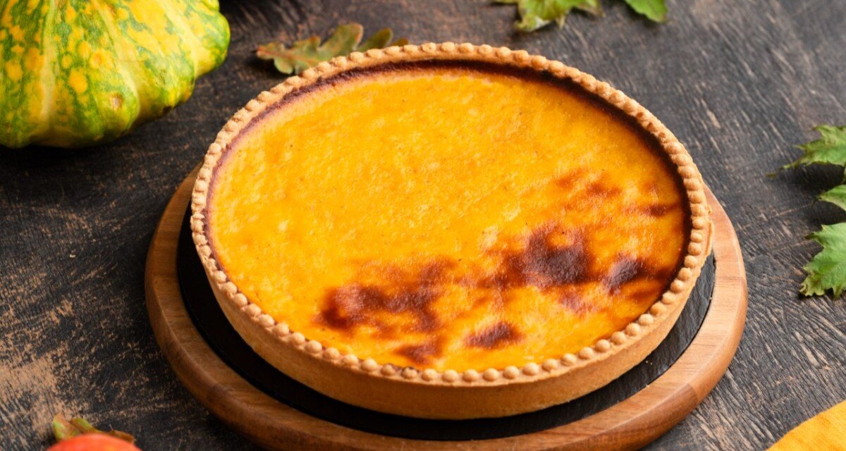 "A beautifully baked squash or pumpkin casserole with a golden-brown crust, surrounded by colorful gourds and autumn leaves on a rustic table.